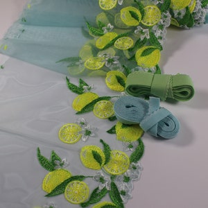 Könnte beinhalten: Hellblauer Tüllstoff mit gelber Zitronenstickerei und grünen Blättern. Zwei Gummibänder sind enthalten, ein grünes und ein hellblaues.