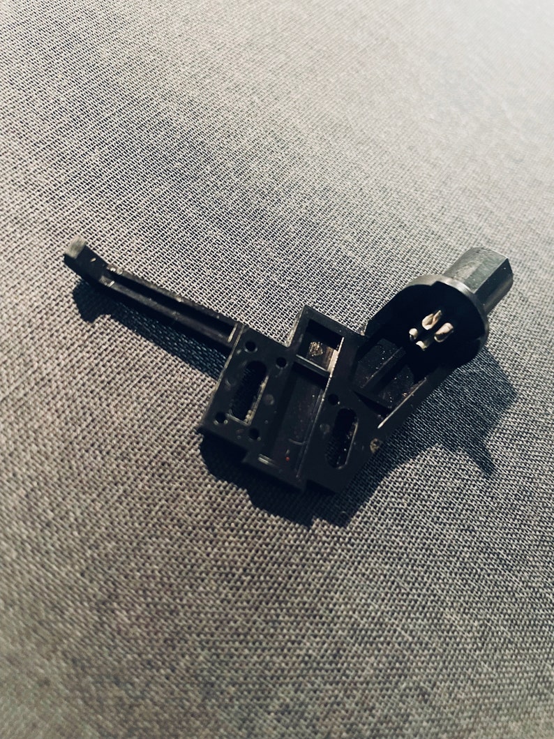 May include: A black plastic component with a lever and a connector. The connector has three prongs. The component is disassembled and lying on a gray fabric surface.