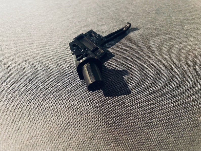 May include: A black plastic part with a lever and a cylindrical piece. The part is designed for a mechanical device.