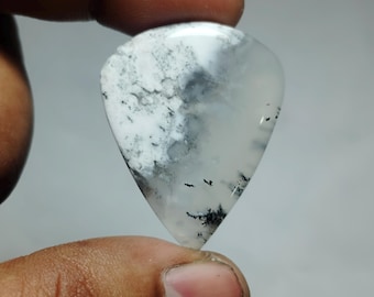May include: A polished, teardrop-shaped gemstone with a white base and intricate patterns of gray and black. The stone is held between fingers, showcasing its smooth, reflective surface and natural variations. The overall aesthetic is organic and elegant.