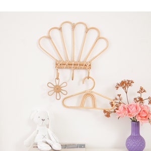 Peut inclure: Un porte-manteau mural en osier blanc avec un crochet en forme de fleur et un cintre en bois. Le porte-manteau est décoré d'un lapin en peluche blanc et d'un vase de fleurs roses.