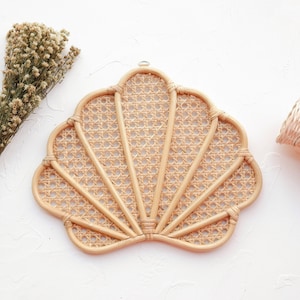 May include: A natural woven rattan wall hanging in the shape of a seashell. The seashell is made of woven rattan and has a light brown color.