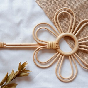 Puede incluir: Un tapiz de pared tejido natural en forma de flor con seis pétalos. La flor está hecha de ratán marrón claro y tiene una abertura circular en el centro.