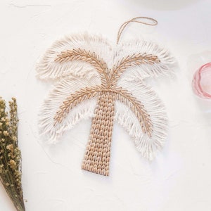 Op de afbeelding: Een witte en bruine macramé palmboom wandhanger. De palmboom is gemaakt van geweven touw en heeft een franje ontwerp.