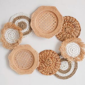 May include: An overhead shot of a collection of woven coasters and placemats in various natural tones. The collection includes round and hexagonal shapes, with textures ranging from tightly woven to fringed edges. The neutral color palette suggests a rustic or bohemian aesthetic.