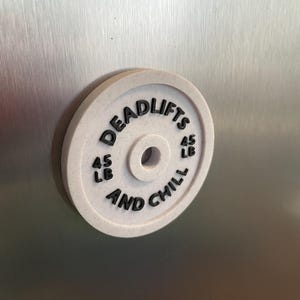 May include: White round weight plate with black text that reads "Deadlifts 45 LB And Chill 45 LB".