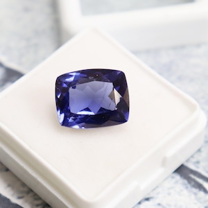 Puede incluir: Una piedra preciosa azul oscuro con corte cojín, expuesta en una caja blanca.