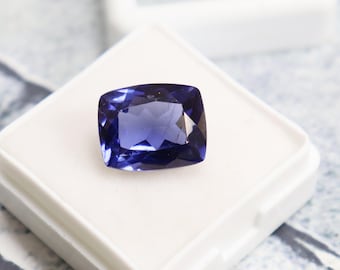 Può includere: Una pietra preziosa blu scuro con taglio a cuscino, esposta in una scatola bianca.