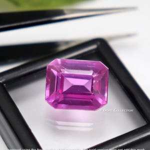 Puede incluir: Una gema rosa vibrante con un corte rectangular esmeralda, exhibida en una caja de joyería de terciopelo negro. © DOPE COLLECTION