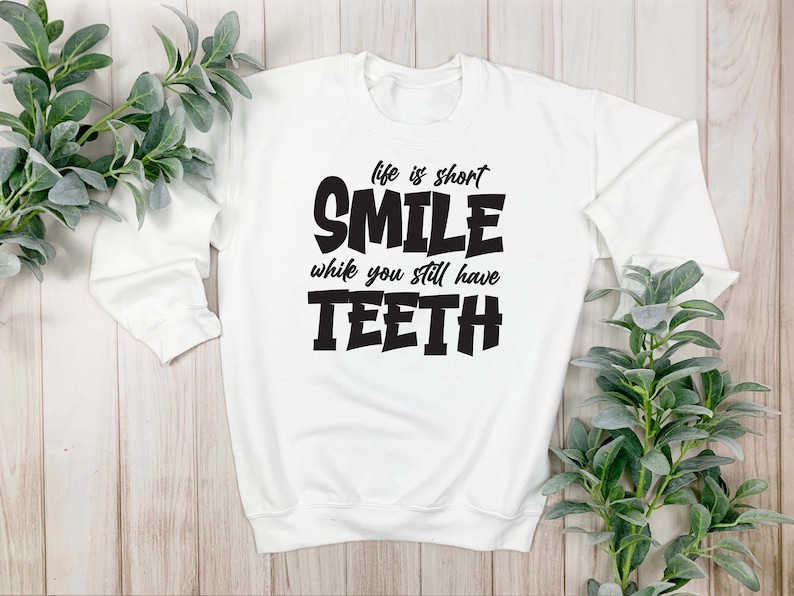 May include: White sweatshirt with black text that reads "Life is short, Smile while you still have Teeth".