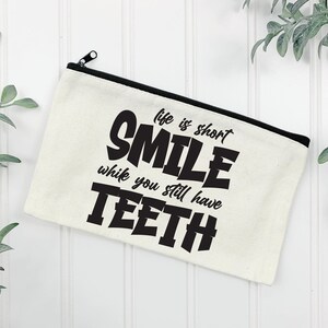 May include: White canvas zippered pouch with black text that reads "Life is short, Smile while you still have teeth."