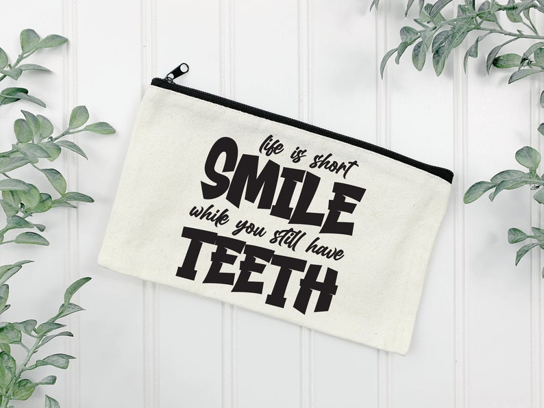 May include: White canvas zippered pouch with black text that reads "Life is short, Smile while you still have teeth."