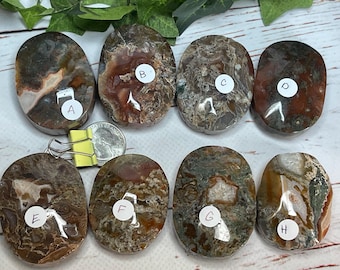 May include: Eight polished, oval-shaped stones with a variety of colors, including brown, red, and green. Each stone has a unique pattern and is labeled with a letter from A to H. A quarter and a binder clip are also in the image.