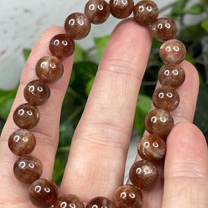 May include: A brown sunstone beaded bracelet with a polished finish. The beads are round and have a slight shimmer.