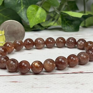 May include: A brown sunstone beaded bracelet with a shiny, metallic finish. The bracelet is made of round beads and is approximately 7 inches in length.