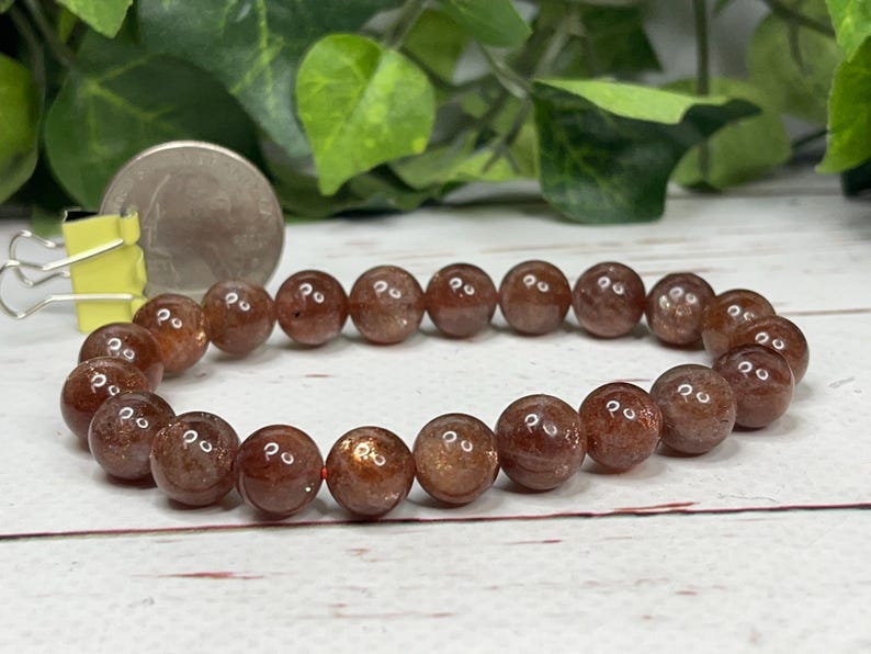 May include: A brown sunstone beaded bracelet with a shiny, metallic finish. The bracelet is made of round beads and is approximately 7 inches in length.