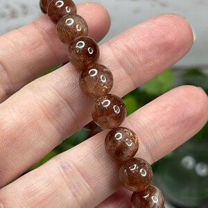 May include: A brown sunstone bracelet with round beads. The beads have a shimmery, iridescent quality.