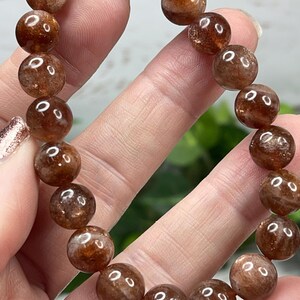 May include: A brown sunstone bracelet with round beads. The beads are translucent and have a shimmery, iridescent quality.