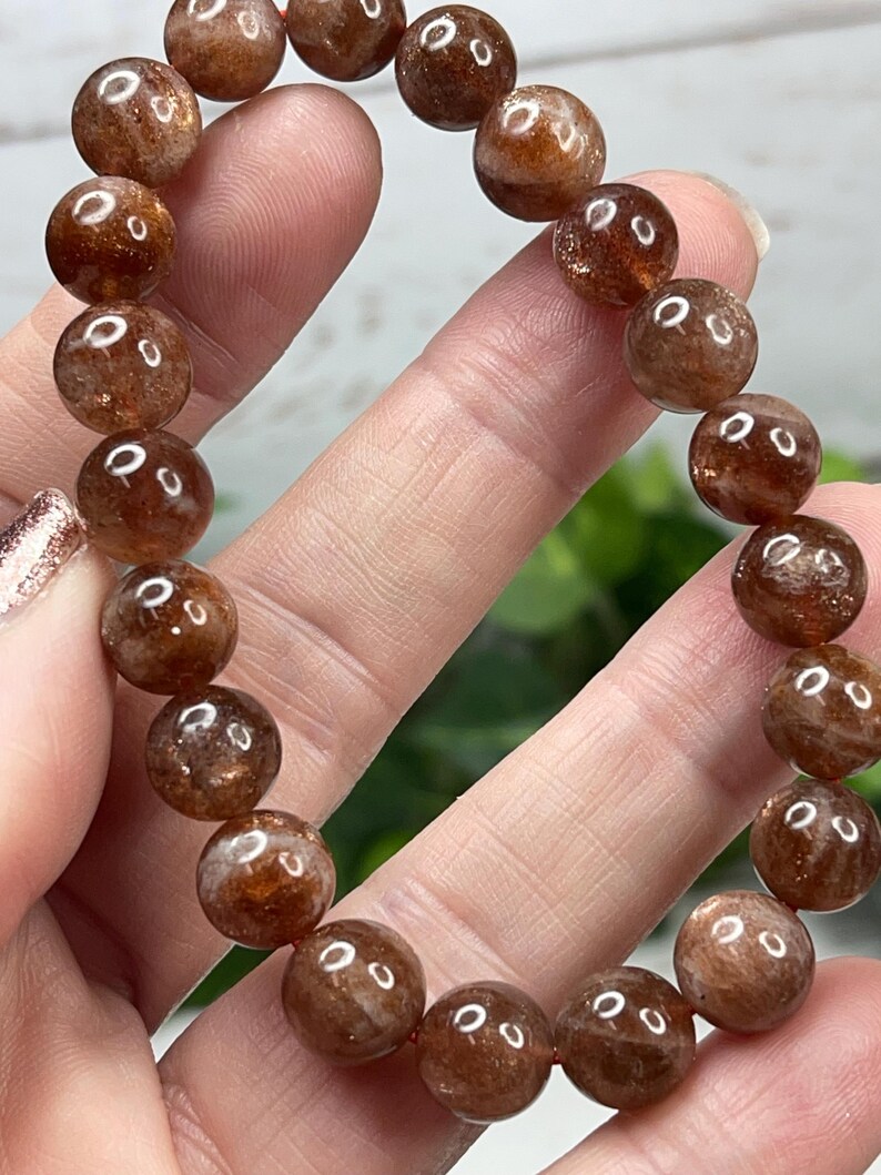 May include: A brown sunstone bracelet with round beads. The beads are translucent and have a shimmery, iridescent quality.