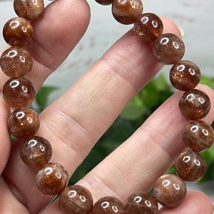 May include: A brown sunstone bracelet with round beads. The beads are translucent and have a shimmery, iridescent quality.