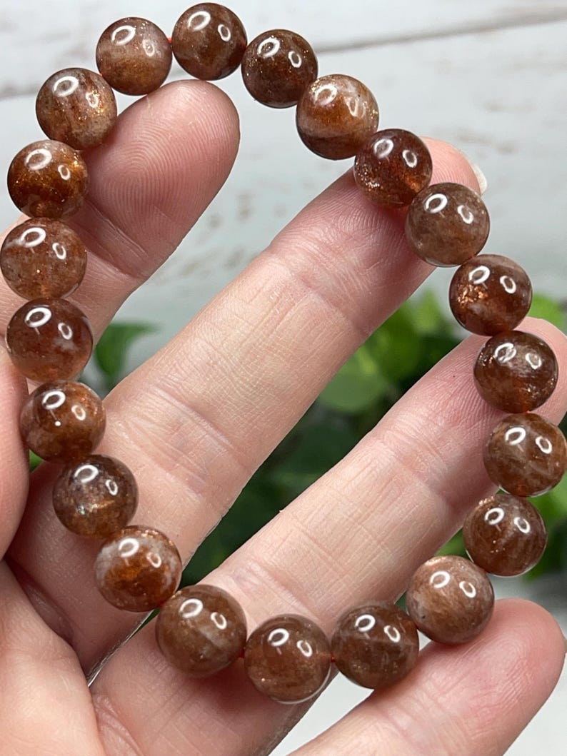 May include: A brown sunstone bracelet with round beads. The beads are translucent and have a shimmery, iridescent quality.