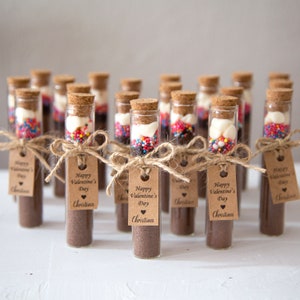 May include: A collection of small glass test tubes filled with hot chocolate mix, marshmallows, and sprinkles. Each tube is tied with twine and a brown paper tag that reads "Happy Valentine's Day Christina".
