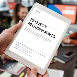 May include: A white tablet displaying a document titled "PROJECT REQUIREMENTS" in bold black text. The document includes fields for client name, supplier name, project name, and project number. A logo is in the top corner.