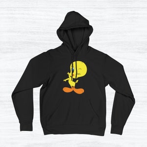 Puede incluir: Sudadera con capucha negra con un p&aacute;jaro amarillo de dibujos animados que lleva un lazo rojo y gui&ntilde;a un ojo. El p&aacute;jaro est&aacute; de pie sobre sus dos pies con las alas extendidas.