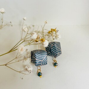 May include: A pair of black and pink geometric patterned earrings with gold accents and black beads hanging from the bottom.