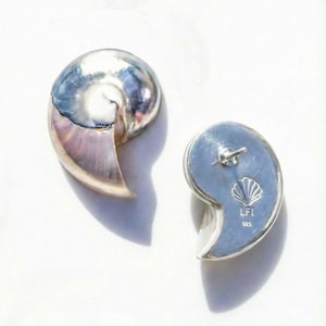 May include: Two silver-colored seashell-shaped earrings. The earrings have a polished, reflective surface with a spiral design. The back of one earring shows a post and a seashell logo with the text "LF1 925".