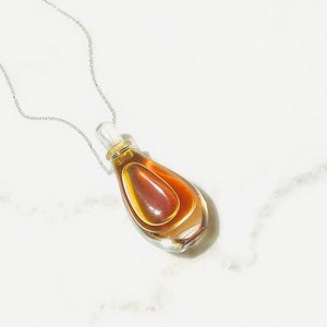 May include: A silver chain necklace with a clear glass bottle pendant filled with a brown liquid.