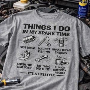 Könnte beinhalten: Ein graues T-Shirt mit dem Text "THINGS I DO IN MY SPARE TIME" und Illustrationen von Werkzeugen und Aktivitäten. Das Shirt enthält Sätze wie "Lose 10mm", "Magnet Fishing" und "Run on Coffee + Regret".