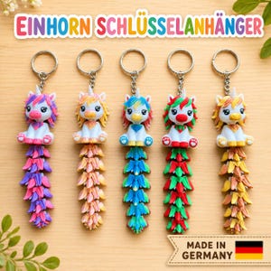May include: Five unicorn keychains with articulated tails, each featuring a white body and colorful hair, mane, and tail segments. The text EINHORN SCHLÜSSELANHÄNGER appears at the top, and a MADE IN GERMANY label with a flag is at the bottom.