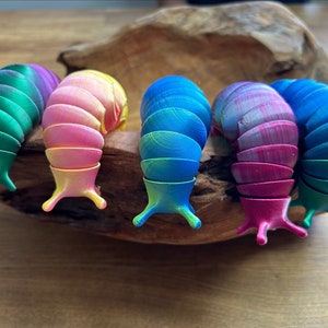 Könnte beinhalten: Fünf bunte, segmentierte Schnecken aus Plastik. Die Schnecken sind grün, rosa, blau, lila und türkis.