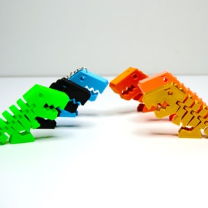 Könnte beinhalten: Vier Plastik-Dinosaurierspielzeuge in verschiedenen Farben: grün, blau, schwarz und gold. Die Dinosaurier sind in einer Reihe angeordnet und einander zugewandt.