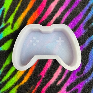 May include: White silicone mold shaped like a video game controller. The mold has a textured surface and is designed for making resin crafts.