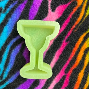May include: A light green silicone mold shaped like a margarita glass. The mold is on a colorful zebra print background.