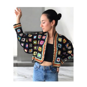 May include: A black crochet cardigan with colorful granny squares. The cardigan has a cropped length and long sleeves. The cardigan is made with a variety of colors, including red, orange, yellow, green, blue, and purple.