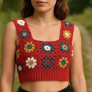 May include: A red crochet top with a square pattern featuring white, yellow, blue, and green flowers. The top is sleeveless and has a square neckline.