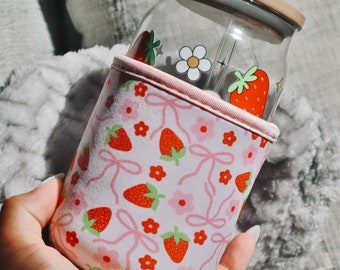 Può includere: Un manicotto isolante per tazza rosa e bianco con un motivo a fragole e fiori. Il manicotto è progettato per adattarsi a una bottiglia di vetro con una cannuccia.