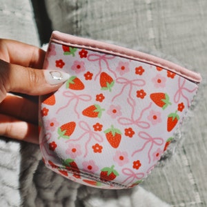 K&ouml;nnte beinhalten: Eine rosa Neopren-Getr&auml;nkedose mit einem Erdbeer- und Schleifenmuster. Die K&uuml;hlbox ist so konzipiert, dass Getr&auml;nke kalt bleiben.