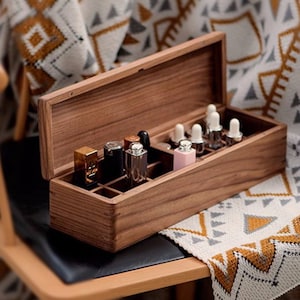 Puede incluir: Una caja de madera con la tapa abierta, que revela compartimentos llenos de pequeñas botellas de varios colores. La caja está sentada en una silla con una manta estampada.