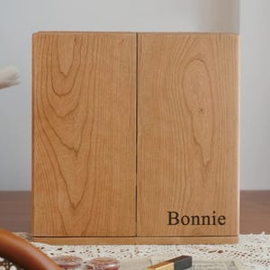 May include: A wooden cabinet with two doors, featuring a natural wood grain pattern. The cabinet is light brown and has the name "Bonnie" printed on the lower right door. The cabinet is sitting on a lace doily.
