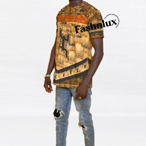 Può includere: Una persona indossa una camicia a maniche corte fantasia con la scritta "Fashnlux" e jeans blu strappati. La camicia presenta un design marrone e oro con dettagli neri. Le scarpe nere completano l'outfit.
