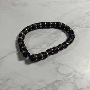 May include: A black and gold beaded bracelet. The bracelet is made of small, round beads with a gold accent on each bead.