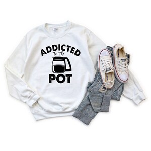 May include: White sweatshirt with black text that reads "Addicted to the Pot" with a black and white illustration of a coffee pot.