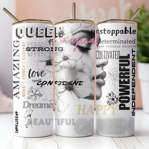 May include: A white tumbler with a black and white illustration of a woman's face and flowers. The tumbler has text that reads "Queen", "Amazing", "Strong", "Love", "Confident", "Dreamer", "Beautiful", "Unstoppable", "Determinated", "Cultivated", "Powerful", "Independent", and "Happy".