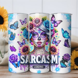 May include: A white stainless steel tumbler with a colorful design featuring a sugar skull with flowers, butterflies, and the text "SARCASM -LOADING-"