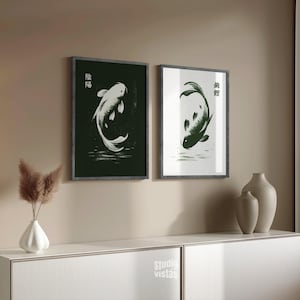 May include: Two framed art prints featuring koi fish illustrations. One print has a white koi on a black background, the other has a green koi on a white background. Both prints have Japanese characters and are displayed above a white cabinet.