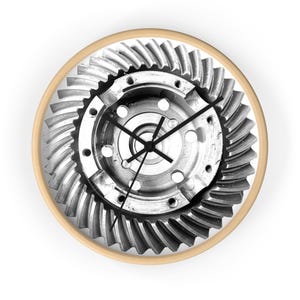 May include: A round wall clock featuring a detailed, grayscale image of a mechanical gear assembly. The clock has a light wood-colored frame and black clock hands. The design showcases industrial and mechanical elements.